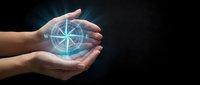 Hands holding glowing digital compass with navigation directions on dark background for business guidance and strategic planning concepts.