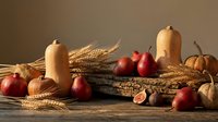 Autumn harvest still life with pumpkins, red apples, wheat stalks, candles and walnuts on rustic wooden table creating warm seasonal atmosphere.