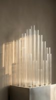 Modern glass tube installation with warm lighting creating geometric shadows on neutral wall for contemporary interior design and architectural projects.