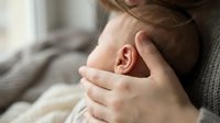 Mother gently holding newborn baby head with tender care showing maternal bond and protection in soft natural light for parenting content.