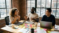 Diverse business team collaborating in modern brick office space with sticky notes and laptops during creative brainstorming session.