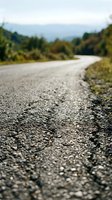 Low angle view of asphalt road surface with blurred forest and mountains in background, suitable for travel, transportation, and journey concepts.