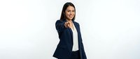 Professional Hispanic businesswoman in navy suit pointing forward with confident smile on white background for corporate presentations and marketing materials.