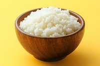 Steamed white rice served in wooden bowl on vibrant yellow background. Fresh cooked jasmine or basmati rice with fluffy texture shows Asian cuisine essentials.
