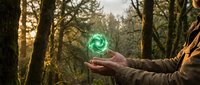 Young adult male with light skin tone holding glowing green swirling energy orb in palm against forest backdrop during golden hour, representing magic, power, nature connection, and spiritual energy for wellness and fantasy concepts.