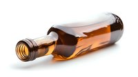 Empty brown glass bottle lying on side with amber liquid spilling out, casting soft shadow on white background, isolated product photography for beverage industry.