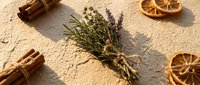 Dried herbs bundle with lavender and rosemary tied with twine, cinnamon sticks and dried orange slices on beige textured surface.