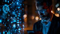 Professional businessman in glasses working late at night with digital technology, illuminated by blue data visualization and ambient city lights, perfect for modern business concepts.