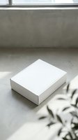 White cardboard box on concrete floor near window with natural light for product packaging mockup and branding presentation.