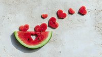 Watermelon slice with heart-shaped cutouts arranged in a flying pattern on light concrete background, perfect for summer food concepts.