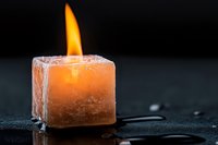 Melting orange wax candle with bright flame on dark wet surface creating atmospheric mood lighting for relaxation and spa treatments.