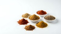 Colorful ground spices in white bowls and scattered piles on clean background for culinary cooking and seasoning recipes.