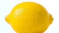Fresh yellow lemon with textured skin isolated on white background, suitable for food and beverage marketing.