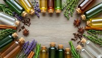 Essential oils in glass bottles arranged in circle with lavender, rosemary and spices on wooden background for aromatherapy and natural wellness treatments.