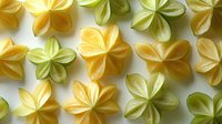 Delicate origami flowers in yellow and green tones arranged on white background create gentle pattern. Decorative paper art elements for craft projects.