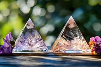 Crystal pyramid shapes with delicate internal formations in pink and purple hues, decorated with flowers against natural bokeh background, spiritual healing concept.