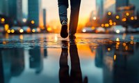 Person walking on wet city street at sunset with reflection in puddle, dramatic urban bokeh lights creating atmospheric mood for lifestyle and travel concepts.