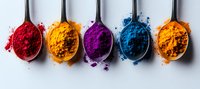 Vibrant spices and natural food coloring powders arranged in silver spoons on light background, including turmeric, paprika and spirulina pigments.