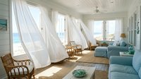 Coastal living room with flowing white curtains, blue upholstered seating, rattan furniture and ocean views through large windows, perfect for interior design and home decor projects.
