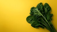 Fresh green leafy vegetables including kale and spinach arranged on bright yellow background with copy space for healthy eating and nutrition concepts.