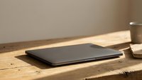 Closed black laptop on wooden desk with warm sunlight and coffee cup, suitable for business, technology, and workspace design projects.