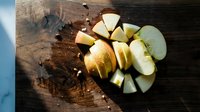 Fresh sliced green apples arranged on rustic wooden cutting board with knife, healthy snacking and food preparation concept for kitchen use.