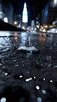 Raindrop splash crown formation on dark wet surface with blurred city lights and skyscraper silhouette in background during night rainfall.