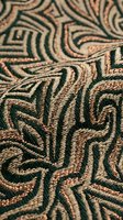 Intricate embroidered textile with geometric patterns in green and gold threads creating ornate decorative fabric surface for luxury interior design projects.