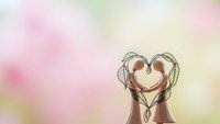 Two women with long flowing hair forming heart shape with heads together on soft pastel rainbow background for love friendship and connection concepts.
