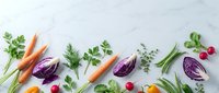 Fresh organic vegetables and herbs arranged on white marble background with copy space for healthy cooking and nutrition concepts.