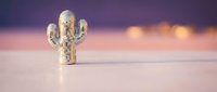 Golden metallic cactus figurine on wooden surface with warm bokeh lights background creating cozy atmospheric home decor scene for interior design.