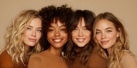 Four diverse young women with different hairstyles smiling together in warm brown tones, representing friendship, beauty and multicultural unity.