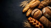 Assorted fresh baked goods including crusty baguettes, round loaves, braided bread and wheat stalks arranged on dark surface for bakery, food and culinary projects.