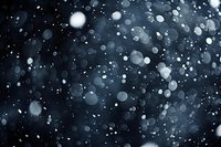 Falling snow at night creates magical bokeh effect against dark background, natural winter precipitation captured in motion with blurred snowflakes.
