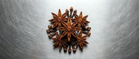 Star anise spices arranged in circular pattern on brushed metal surface for culinary cooking and food photography projects.