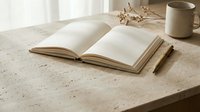 Open notebook with blank pages on textured stone desk, styled with dried flowers and ceramic cup for writing, journaling, and creative workspace design projects.