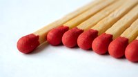 Red wooden matchsticks with sulfur heads arranged in row on white background. Fire starter tools for lighting candles, fireplaces and camping needs.