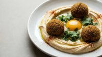 Creamy hummus topped with crispy falafel balls, fresh herbs and olive oil drizzle served on white plate for Mediterranean cuisine and healthy eating.