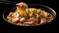 Steaming hot Asian noodle soup with tender chicken pieces, fresh scallions and chili in black ceramic bowl, chopsticks lifting noodles showing texture.
