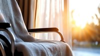 Cozy armchair by window with warm sunlight streaming through sheer curtains, creating peaceful home atmosphere for relaxation or reading.