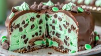 Chocolate-coated mint dessert with layers of green cream filling and chocolate cookie crumbs, cut to show interior texture and decorated with mint meringue peaks.