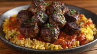 Savory meatballs with fresh herbs served over seasoned rice pilaf with tomatoes in rustic cast iron skillet for Mediterranean cuisine and comfort food recipes.