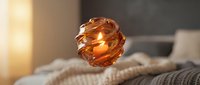 Amber crystal sphere glowing with warm light on cozy knit fabric, creating ambient home decor atmosphere for interior design and lifestyle projects.