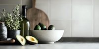 Fresh avocados in concrete bowl with rosemary plant and wine bottle on dark countertop, moody minimalist kitchen styling for food photography.