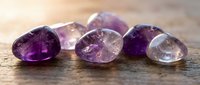 Collection of polished amethyst gemstones in various purple shades arranged on rustic wooden surface for jewelry making and crystal healing practices.