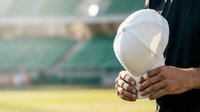 Construction worker holding white safety helmet on outdoor job site with blurred industrial background, representing workplace safety and professional engineering.