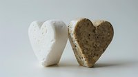 Two heart-shaped stones on white background, one pure white and one speckled gray, symbolizing love, unity and natural contrast in minimalist composition.