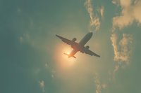 Silhouette of passenger airplane flying against dramatic sunset sky with glowing sun and scattered clouds, creating atmospheric travel scene.