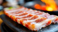 Sliced bacon strips cooking on a dark skillet with flames visible in the background, showcasing crispy, golden-brown meat for culinary and food preparation content.