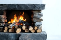 Cozy stone fireplace with burning logs and bright flames creating warm atmosphere against white wall background.